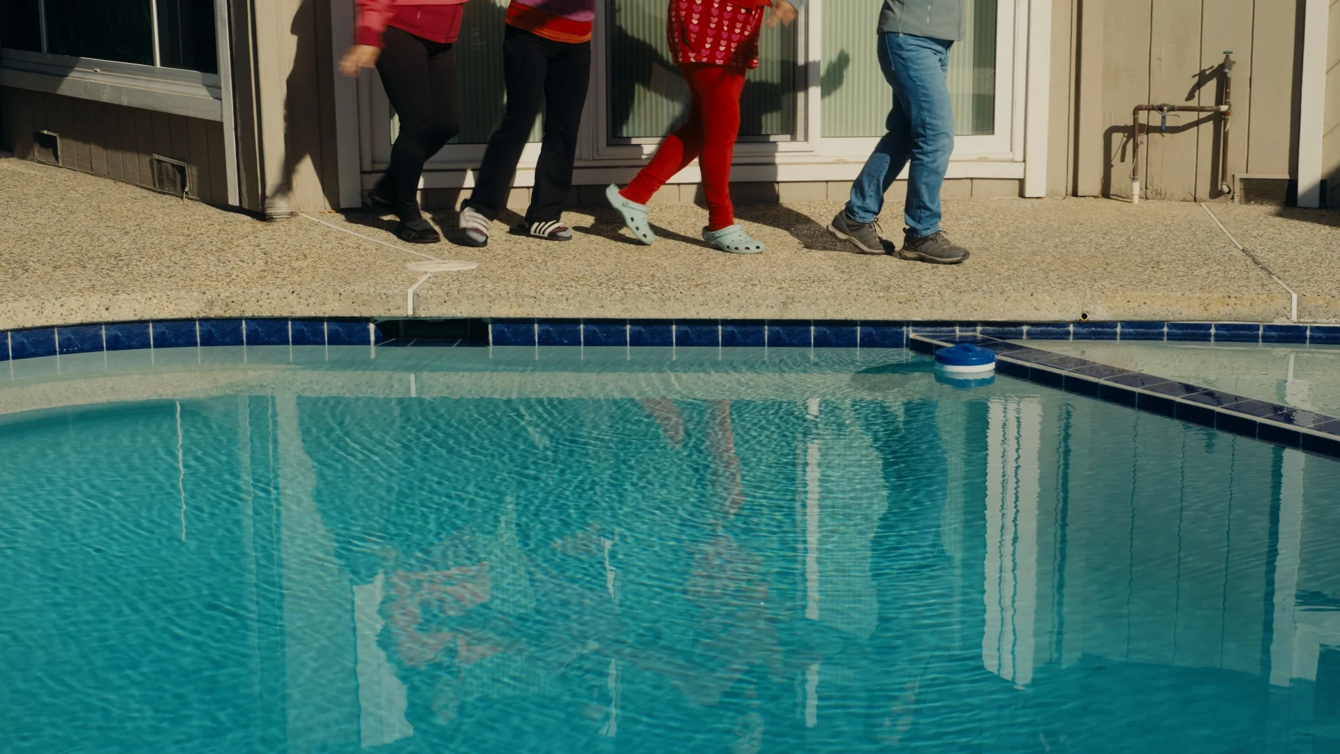 still shot from WHEN ARE YOU COMING HOME? people prance joyously next to a pool