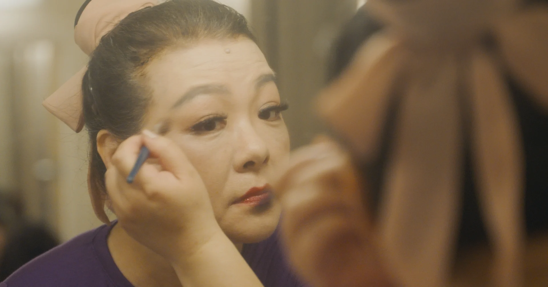 still shot from WHEN ARE YOU COMING HOME? a woman applies her performance makeup