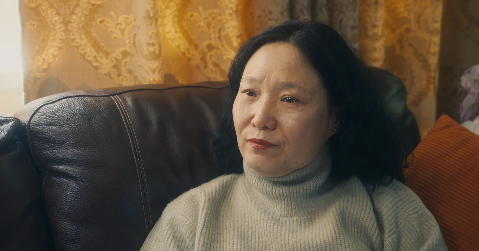 still shot from WHEN ARE YOU COMING HOME? a woman sits on her couch